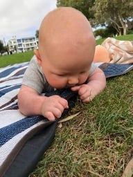 a baby grasping the edge of a blanket during tummy time in a grassy park